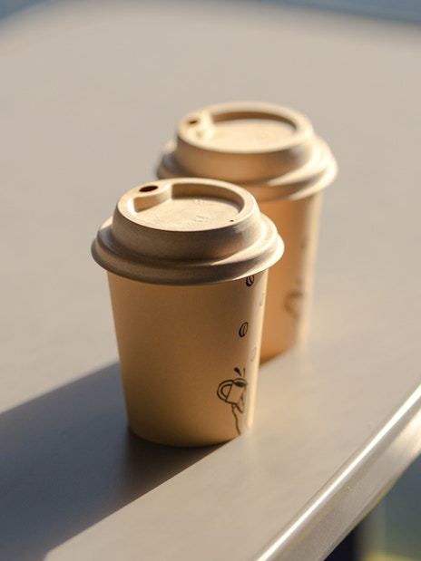 Two paper coffee cups with lids on a table.