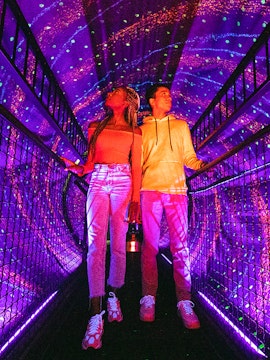 Visitors exploring a colorful light tunnel at Illuseum Berlin.