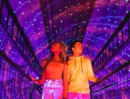 Visitors exploring a colorful light tunnel at Illuseum Berlin.