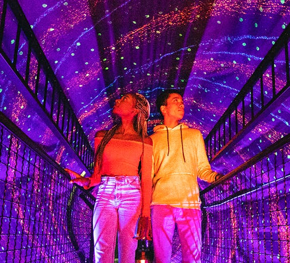 Visitors exploring a colorful light tunnel at Illuseum Berlin.