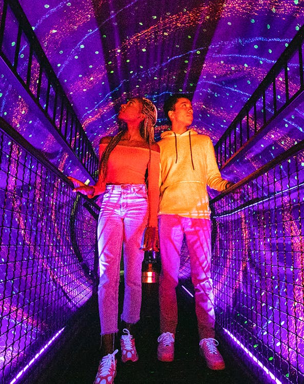Visitors exploring a colorful light tunnel at Illuseum Berlin.