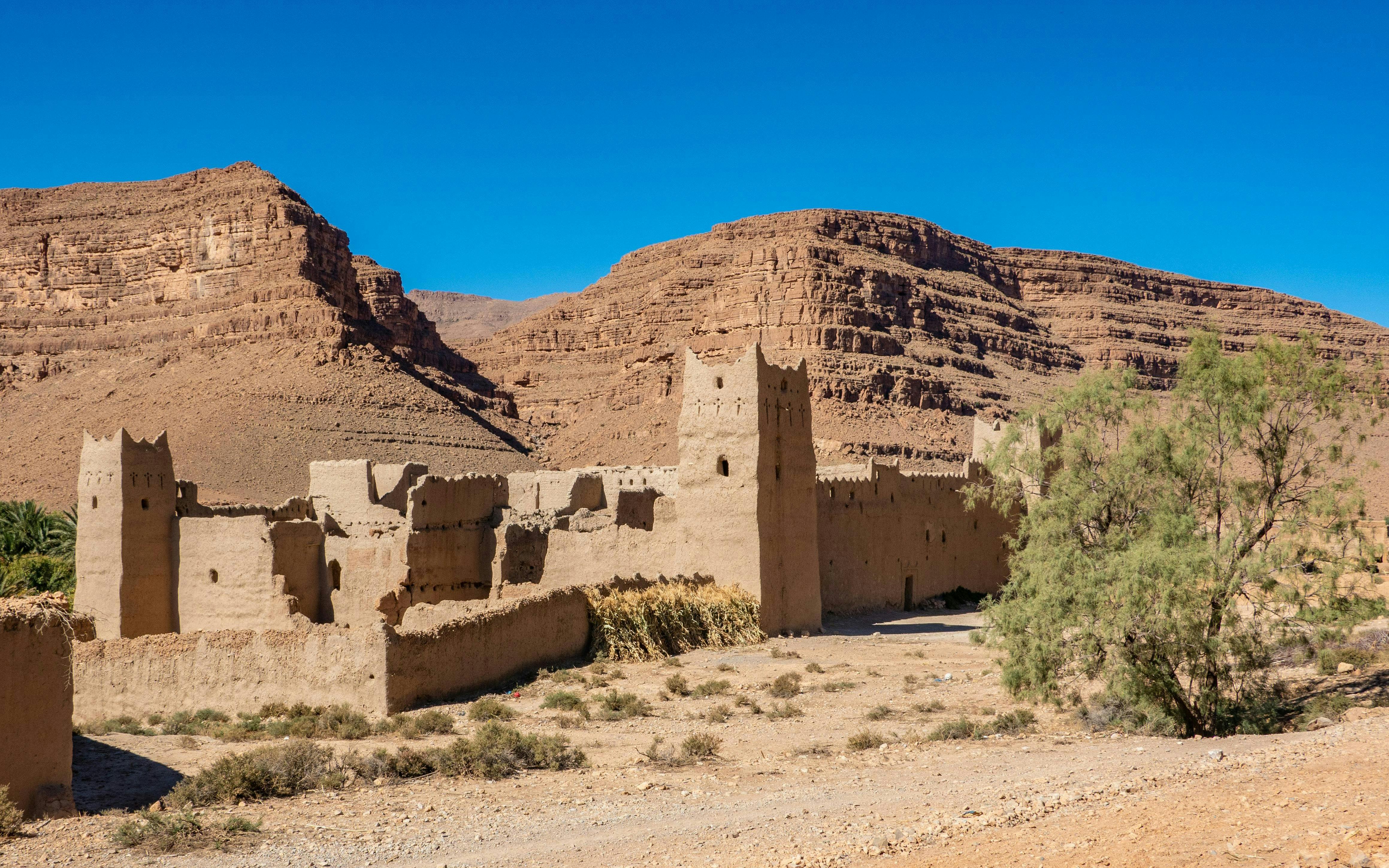 Traditional Kasbah in Ziz Valley, Morocco with desert landscape and mountains.