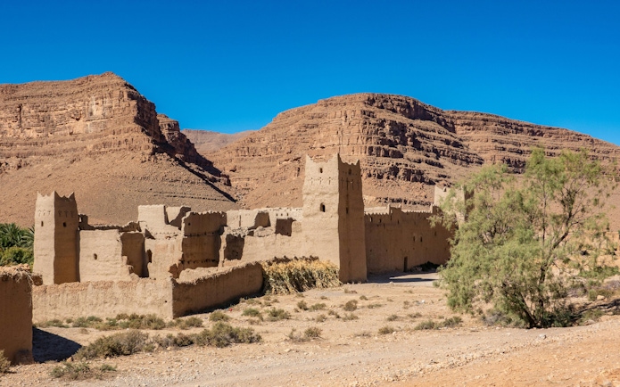 Traditional Kasbah in Ziz Valley, Morocco with desert landscape and mountains.