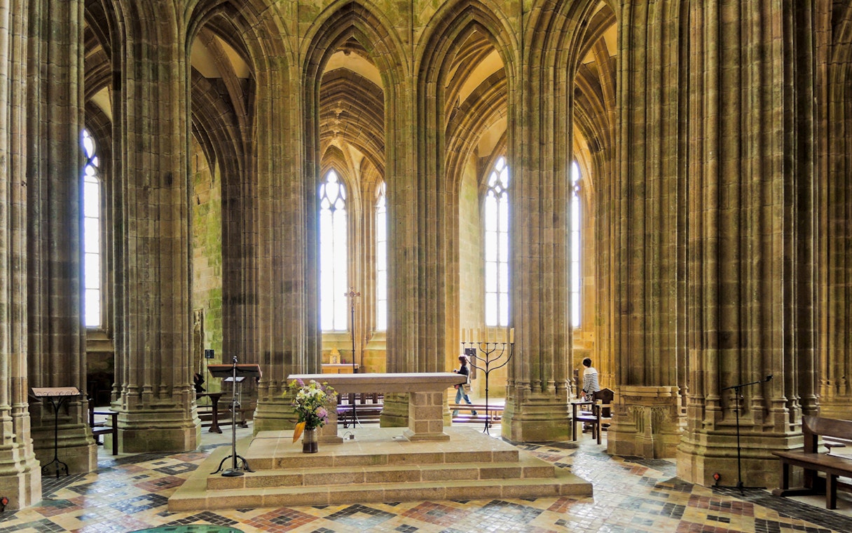 Mont Saint Michel abbey church interior with stone arches, columns, and altar.