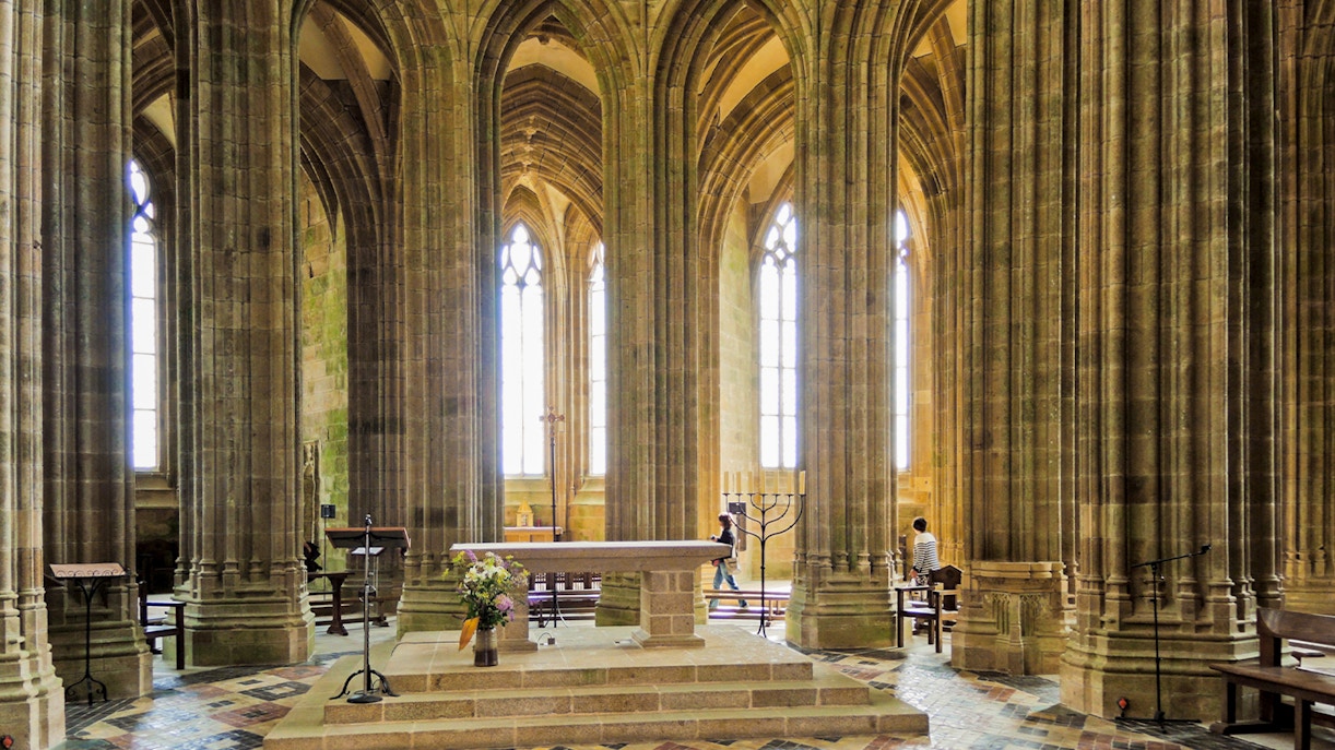 Mont Saint Michel abbey church interior with stone arches, columns, and altar.