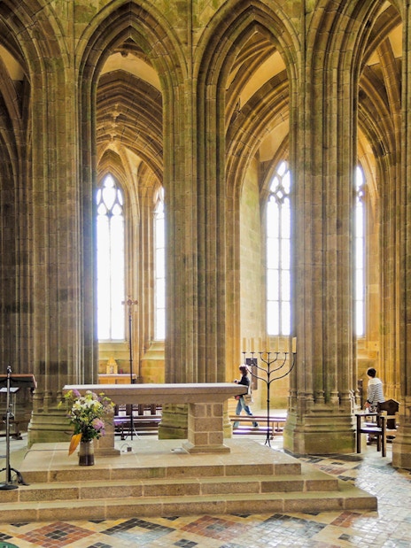 Mont Saint Michel abbey church interior with stone arches, columns, and altar.