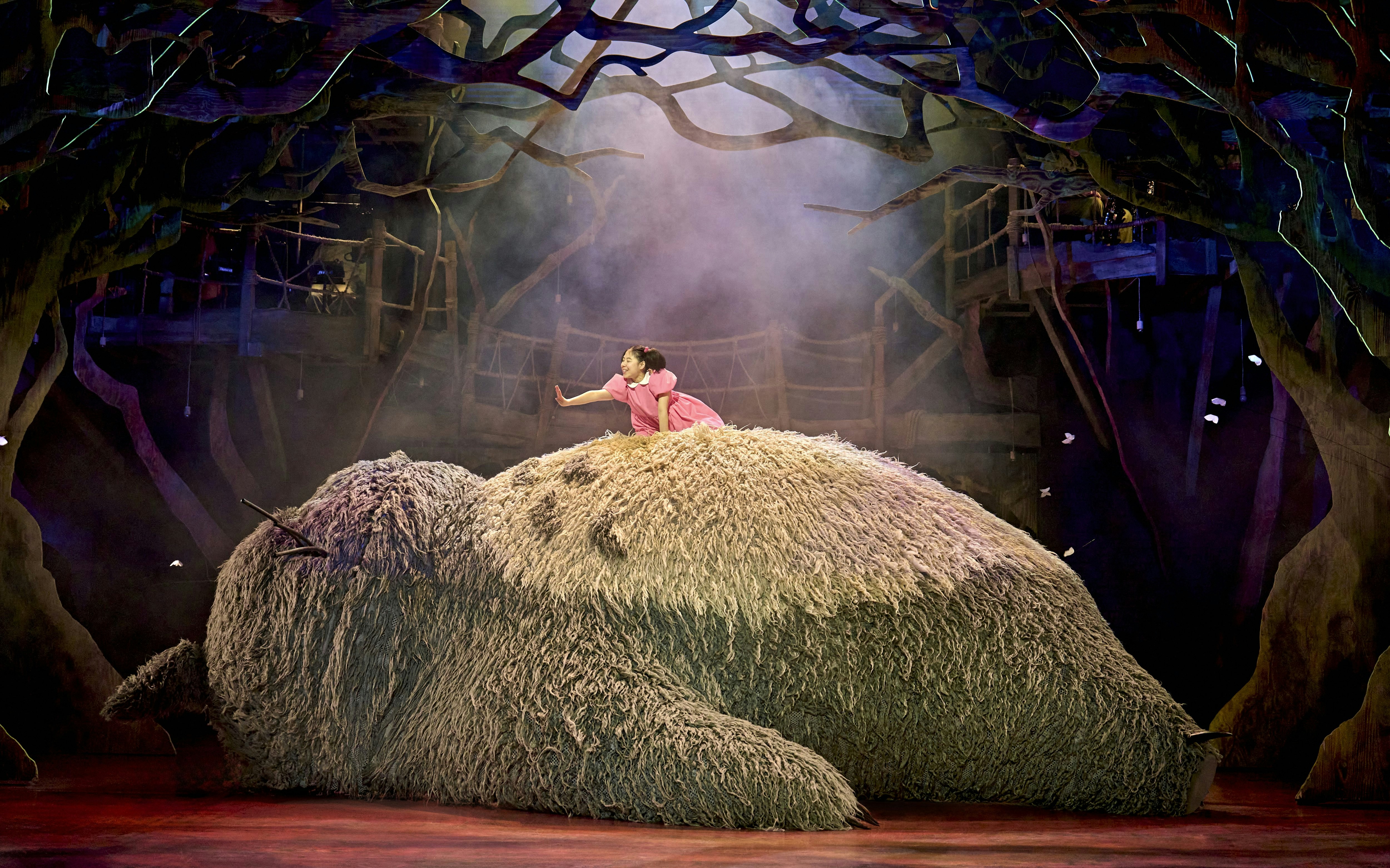 Child on Totoro's back in a forest setting during My Neighbour Totoro stage production.