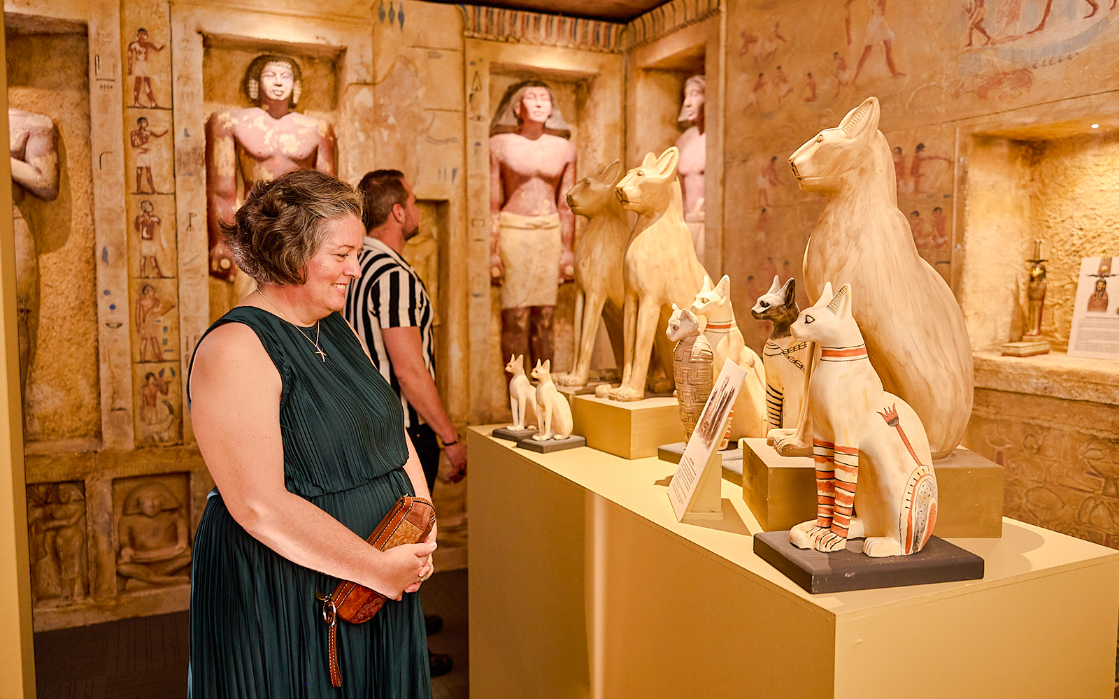 Visitors admire Egyptian cat statues in a museum exhibit.