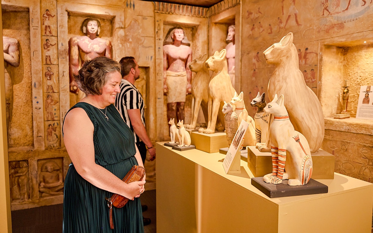Visitors admire Egyptian cat statues in a museum exhibit.