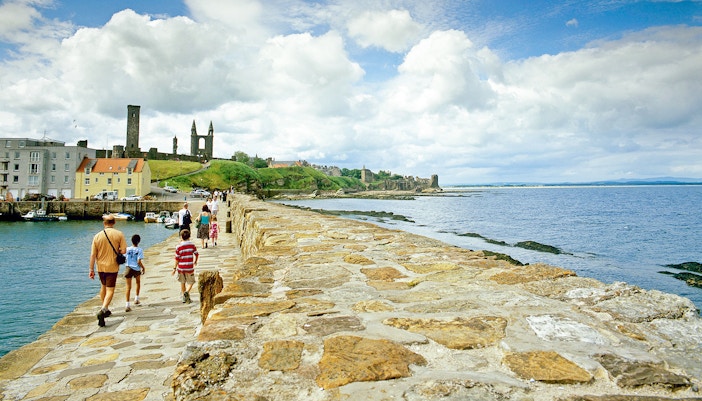 Tourists on coastal path near St. Andrews Cathedral ruins, Scotland.