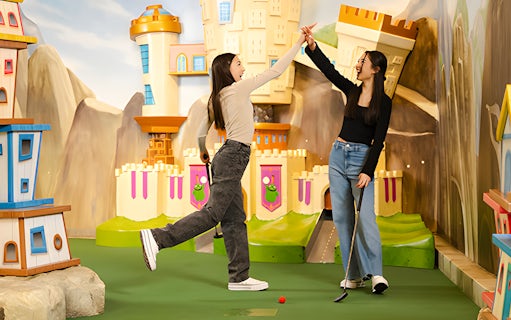 Two people high-fiving at Angry Birds Mini Golf, American Dream, with colorful castle backdrop.