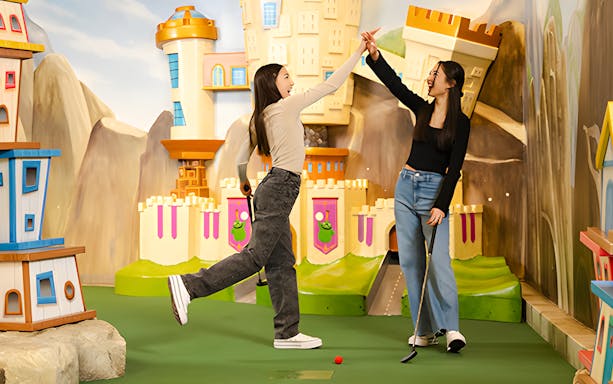 Two people high-fiving at Angry Birds Mini Golf, American Dream, with colorful castle backdrop.