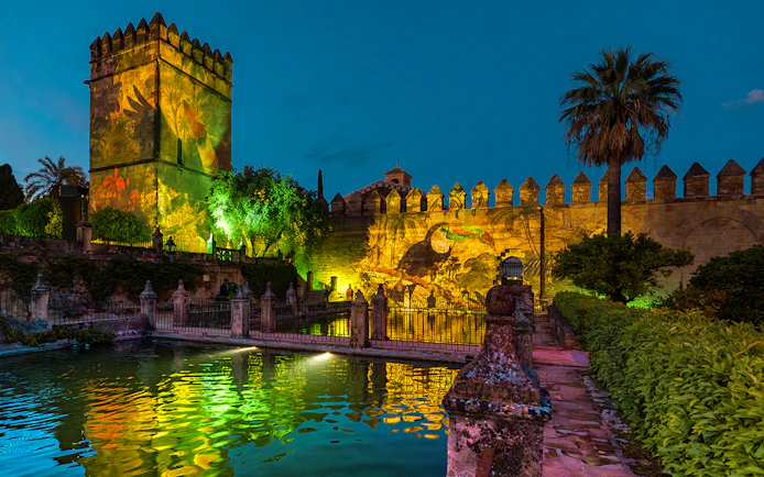 Alcazar of Cordoba garden illuminated at night with colorful reflections in the water.