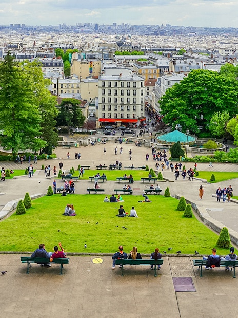 Visitors relaxing on benches in Montmartre with a view of Paris, near Sacré Coeur.