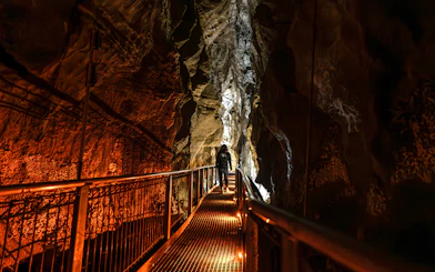 Person walking on a lit pathway inside Ruakuri Cave, New Zealand.