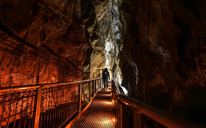Person walking on a lit pathway inside Ruakuri Cave, New Zealand.