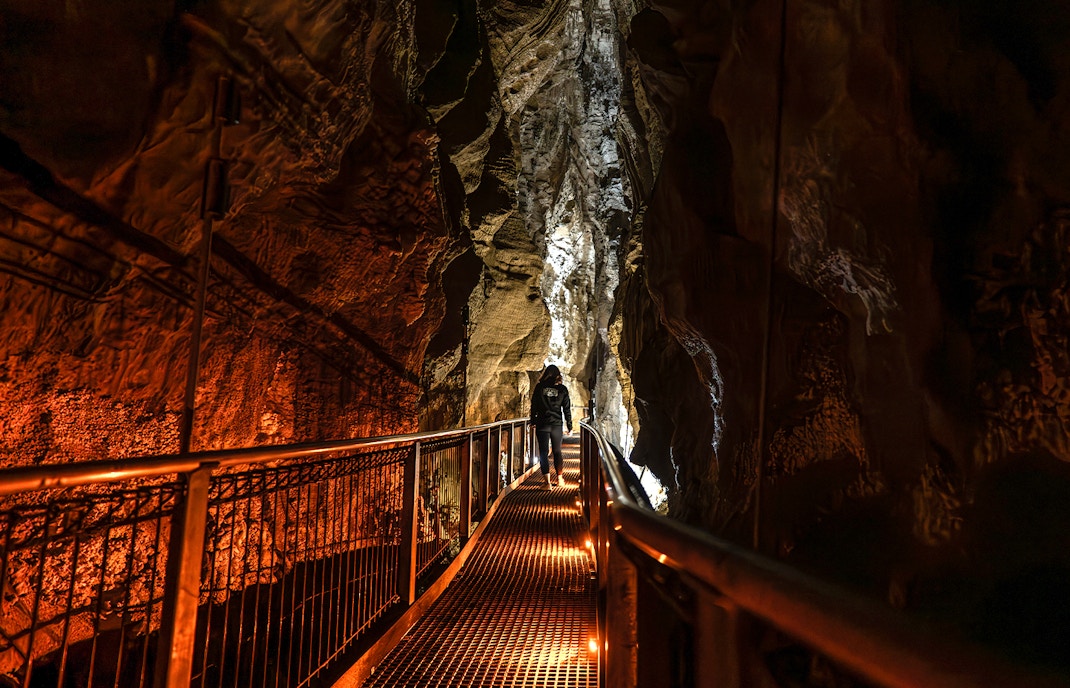 Person walking on a lit pathway inside Ruakuri Cave, New Zealand.