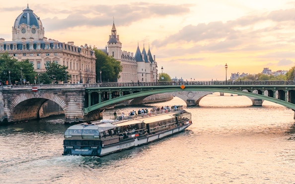 Seine River cruise boat passing under a bridge in Paris at sunset.