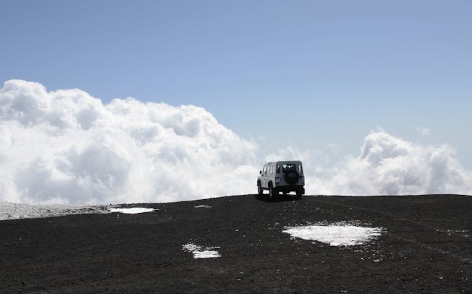 Off-road vehicle on Mount Etna with clouds in the background.