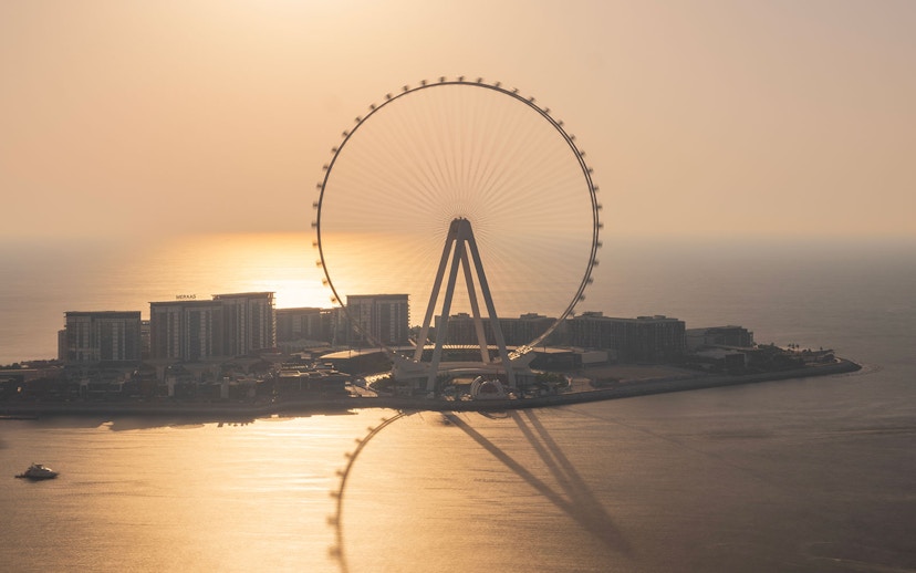 Ain Dubai Ferris wheel silhouetted against a sunset over the sea.