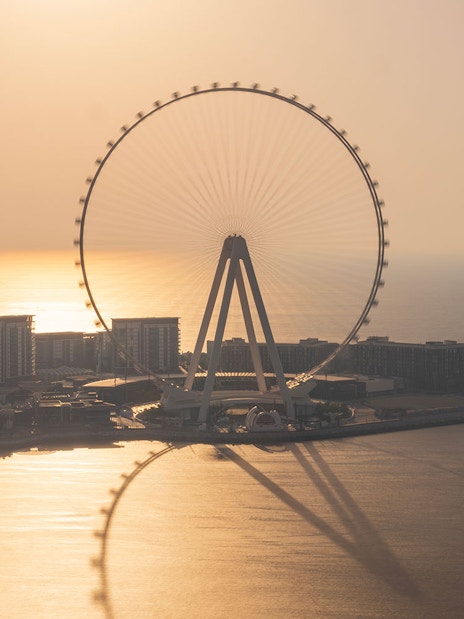 Ain Dubai Ferris wheel silhouetted against a sunset over the sea.
