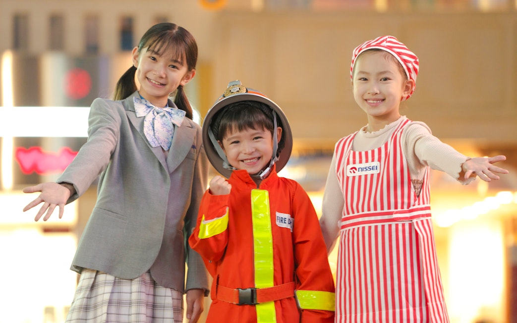 Kids in costumes at KidZania Tokyo, including a firefighter and a chef.
