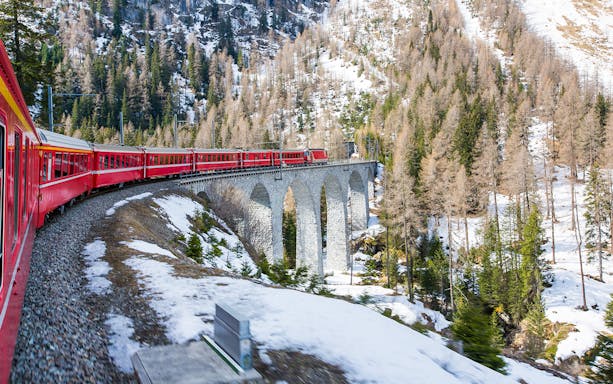 Bernina train crossing a stone viaduct in a snowy alpine landscape.