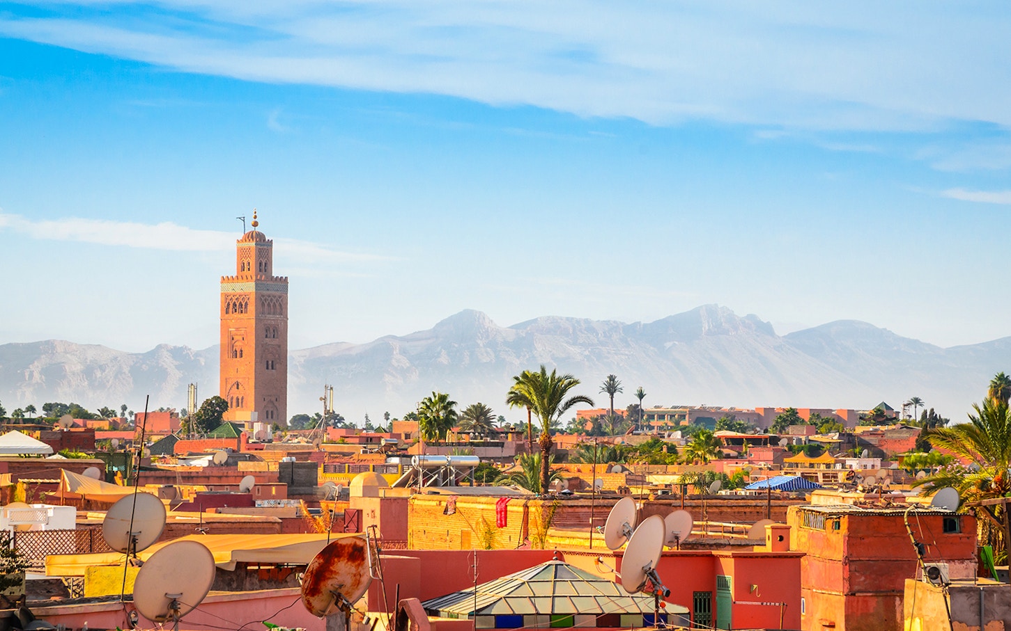 Marrakesh cityscape with Koutoubia Mosque and Atlas Mountains in the background.