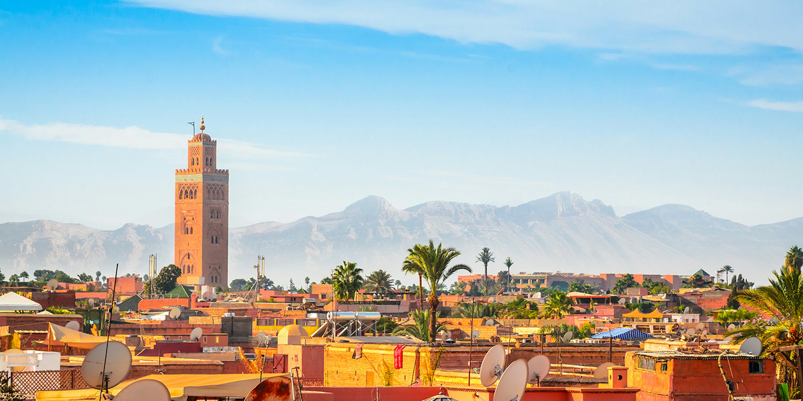 Marrakesh cityscape with Koutoubia Mosque and Atlas Mountains in the background.