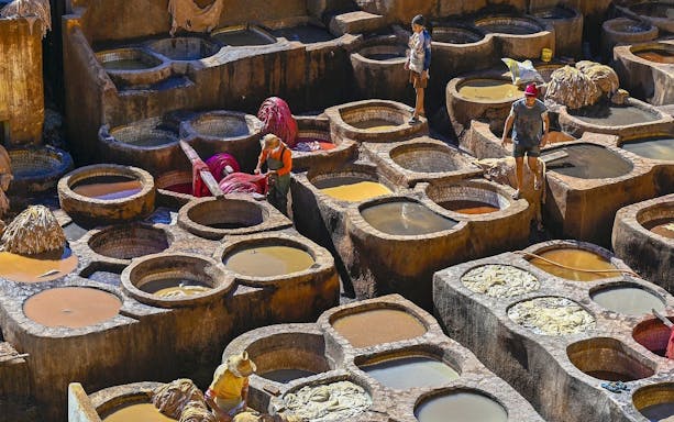 Tannery workers at Chouara Tannery in Fes Old Medina, Morocco, dyeing leather in stone vats.