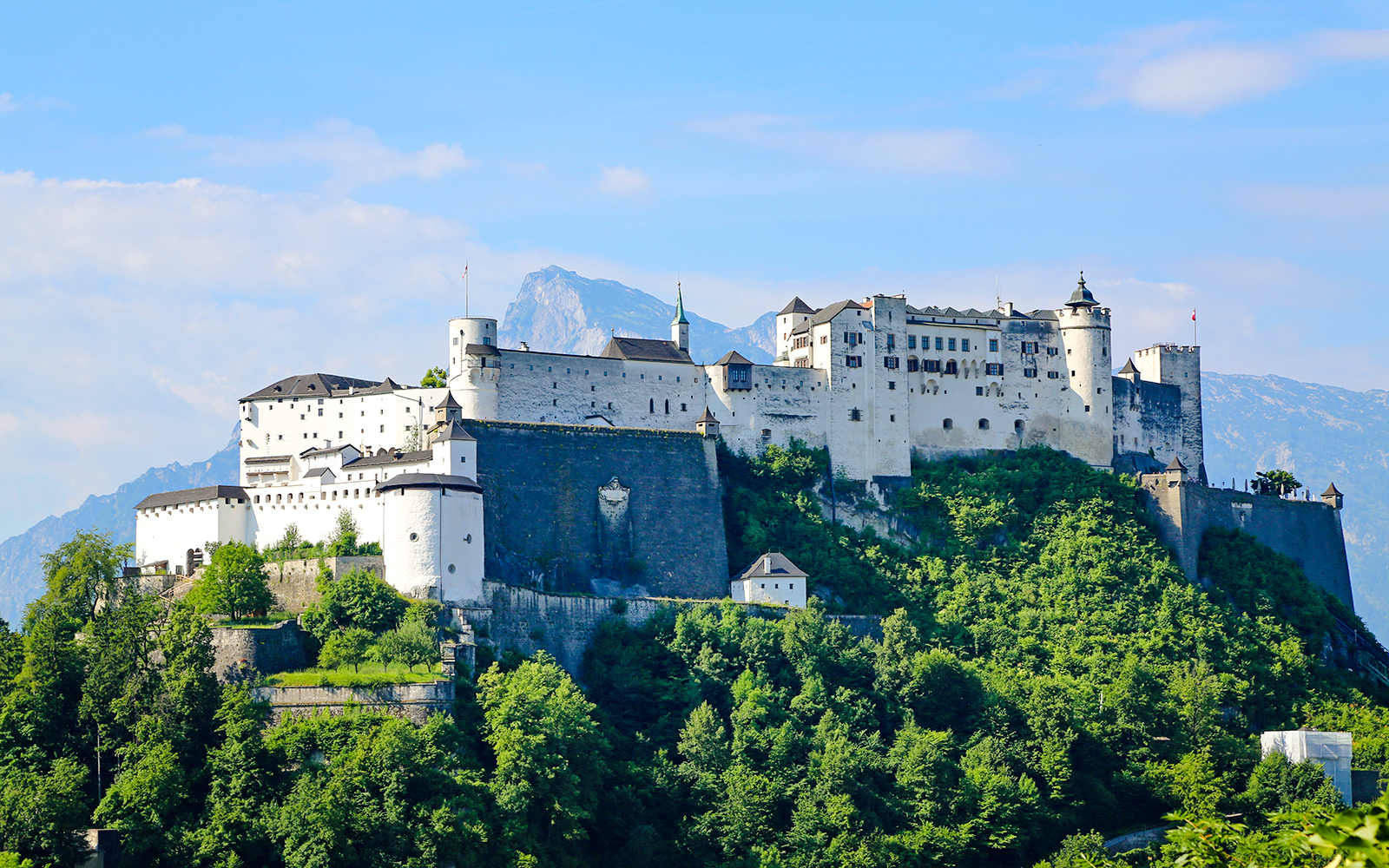 Hohensalzburg Fortress on a hilltop in Salzburg, Austria, surrounded by lush greenery.