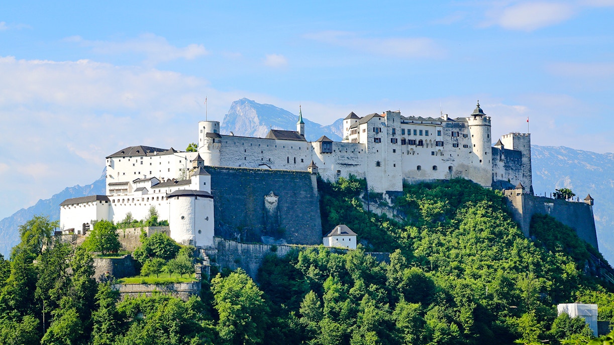 Hohensalzburg Fortress on a hilltop in Salzburg, Austria, surrounded by lush greenery.