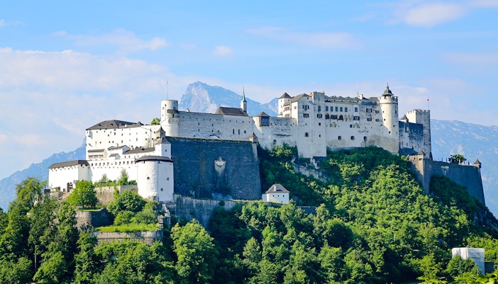 Hohensalzburg Fortress on a hilltop in Salzburg, Austria, surrounded by lush greenery.