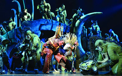 Lion King performance with actors in vibrant costumes on West End stage.