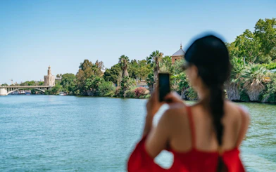 Tourist photographing Torre del Oro from Guadalquivir River cruise in Seville, Spain.