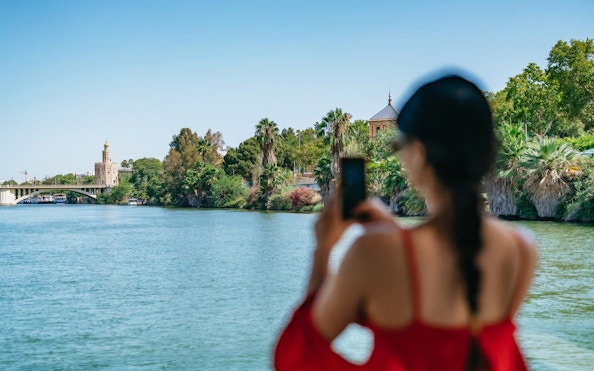Tourist photographing Torre del Oro from Guadalquivir River cruise in Seville, Spain.