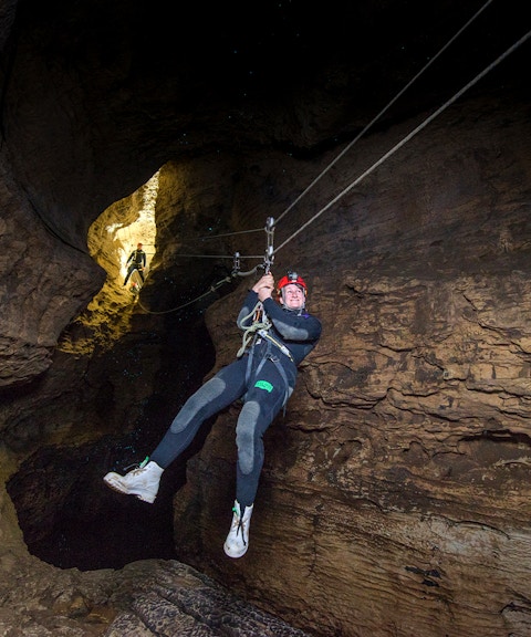Person ziplining through a cave during a Black Water Rafting experience in Waitomo.