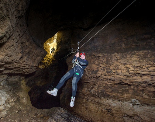 Person ziplining through a cave during a Black Water Rafting experience in Waitomo.