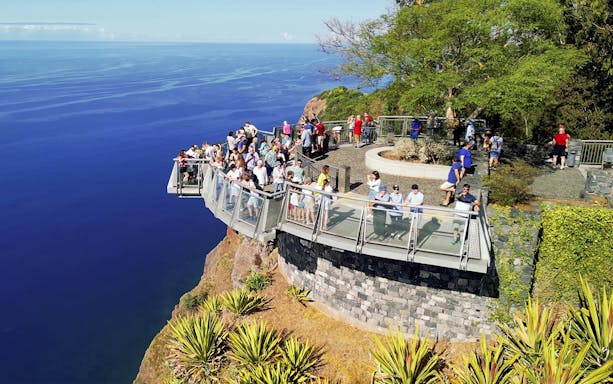 Visitors on a cliffside skywalk overlooking the ocean, part of a wine experience tour.