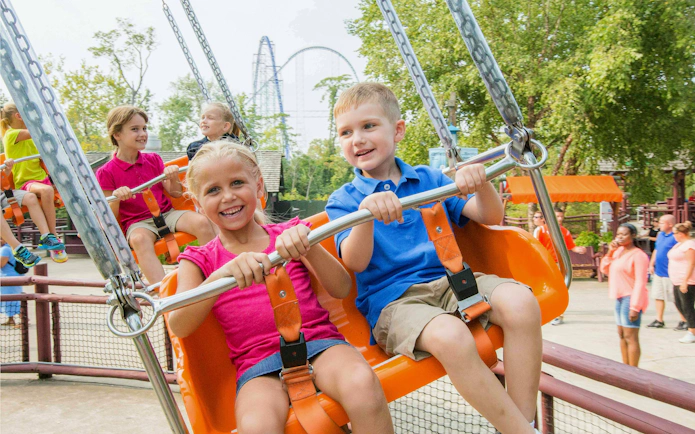 Children enjoying Charlie Brown's™ Wind-Up ride at Cedar Point with roller coaster in background.