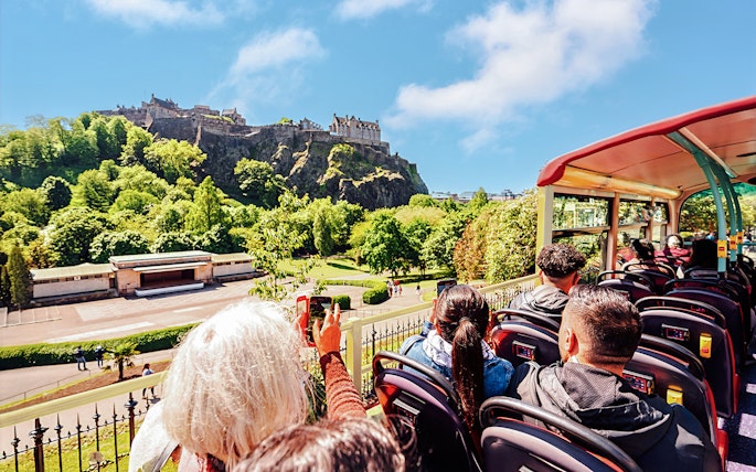 Open-top bus tour with view of Edinburgh Castle in the background.