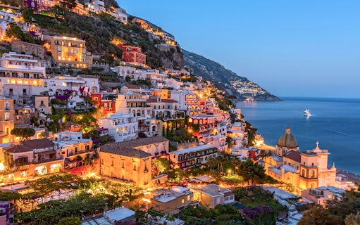 Amalfi Coast hillside view with illuminated buildings and sea, part of Naples day tour.