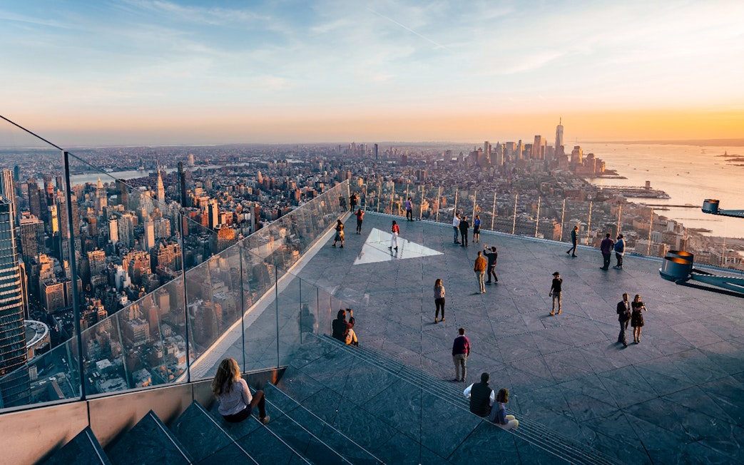 Observation deck view of New York City skyline at sunset, featuring visitors enjoying the scenery.