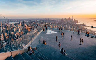 Observation deck view of New York City skyline at sunset, featuring visitors enjoying the scenery.