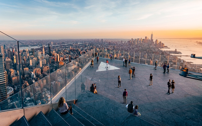 Observation deck view of New York City skyline at sunset, featuring visitors enjoying the scenery.