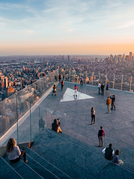 Observation deck view of New York City skyline at sunset, featuring visitors enjoying the scenery.