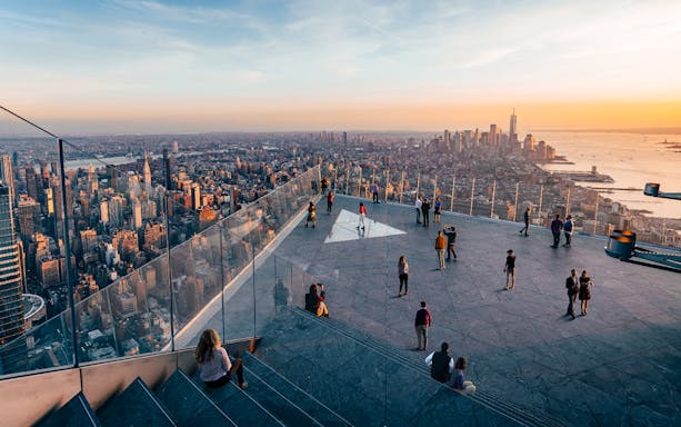 Observation deck view of New York City skyline at sunset, featuring visitors enjoying the scenery.