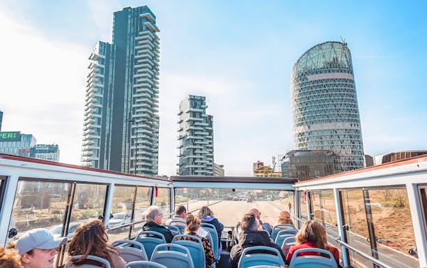 Open-top bus tour in Milan with modern skyscrapers in the background.