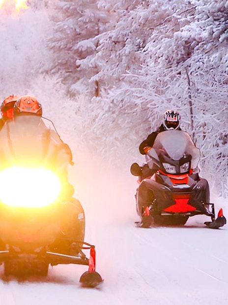 Snowmobilers riding through snowy forest during 1-Hour Snowmobile Safari Adventure from Rovaniemi.