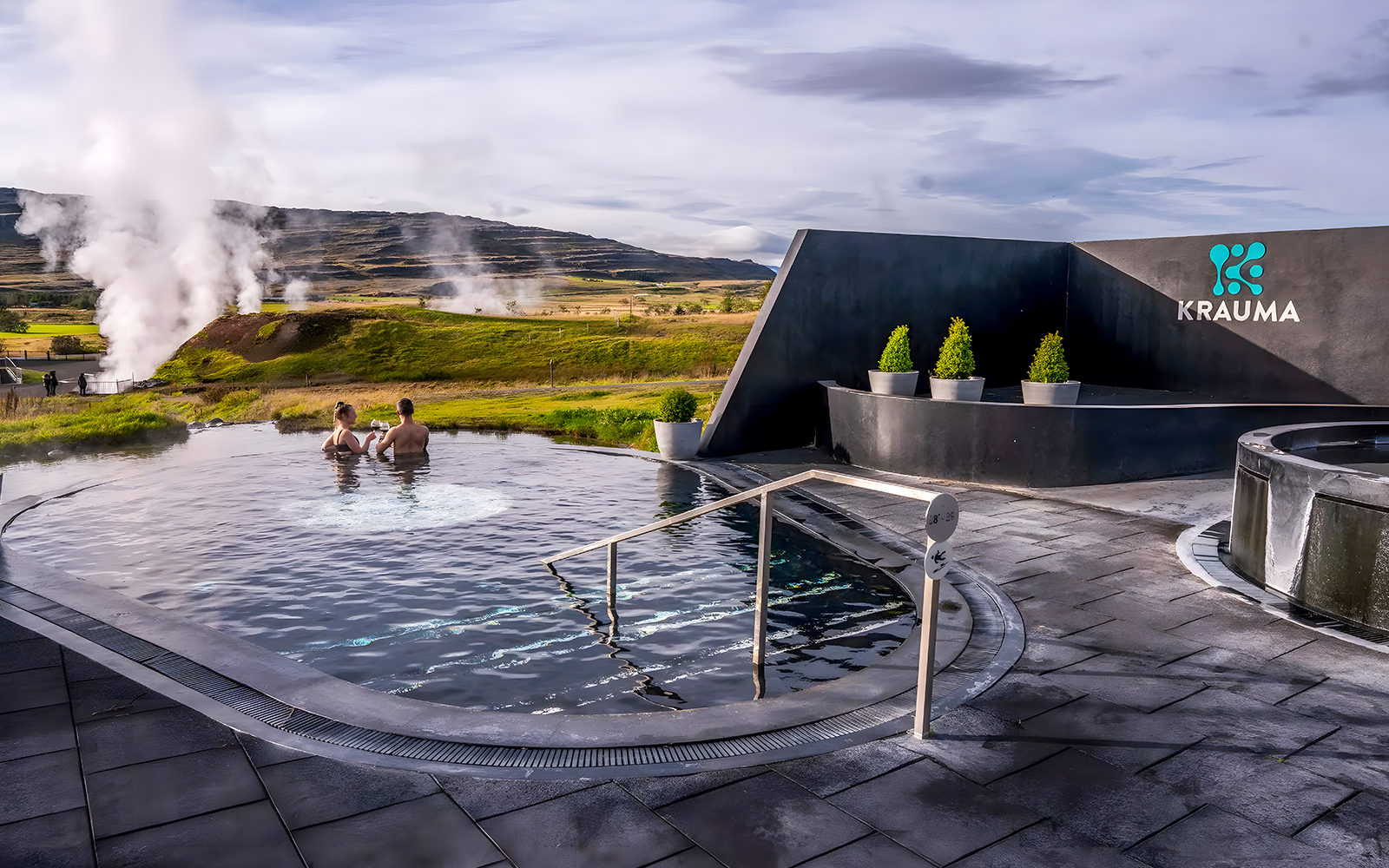 Visitors relaxing in Krauma Geothermal Baths with steam rising in the Icelandic landscape.
